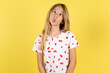 © Roquillo - blonde kid girl wearing polka dot shirt over yellow studio background making fish face with lips, crazy and comical gesture. Funny expression.