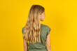 The back side view of a blonde kid girl wearing green T-shirt over yellow studio background . Studio Shoot.