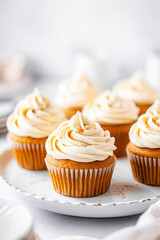 Wall Mural - Pumpkin cupcakes on a white table topped with cream cheese frosting and dusted with cinnamon, generative AI