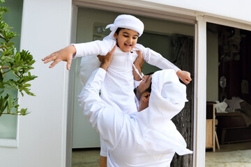 Middle Eastern Arab family father and son together. Arabic boy playing with dad flying in the air. Saudi, Emirati, Qatari, Omani, Kuwaiti nationals spending time at home. Arab man with kid.