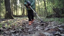 A Man Is Looking For Metal With A Metal Detector. A Guy With A Metal Detector Is Looking For A Treasure Against The Background Of The Forest.