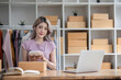 © wichayada - Female online seller preparing delivery items and using calculator to calculate orders