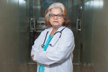 Medical concept, Indian senior female doctor in white coat with stethoscope standing at hospital.