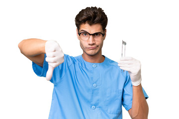 Wall Mural - Young dentist man holding tools over isolated background showing thumb down with negative expression