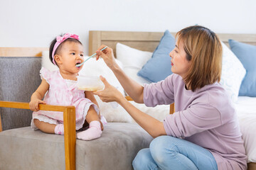 Asian mother is feeding infant formula to her cute toddler baby girl for healthy kid nutrition and motherhood by raising child to grow and parenting concept