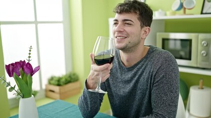 Wall Mural - Young hispanic man drinking glass of wine sitting on table at dinning room