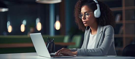 Leinwandbilder - Black woman taking notes during office webinar using laptop and wearing headphones with empty space