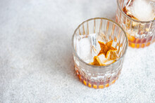 Glasses Of Whiskey With Ice And Orange Peel On Gray Surface