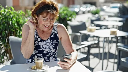 Poster - Middle age woman using smartphone with winner gesture at coffee shop terrace