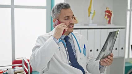 Canvas Print - Young hispanic man doctor looking xray talking on smartphone at clinic