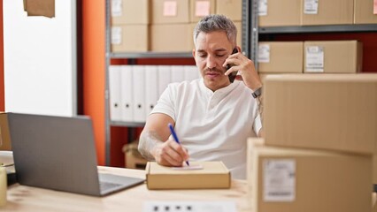 Poster - Young hispanic man ecommerce business worker talking on smartphone writing on package at office