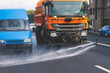 Municipal watering truck machines washes asphalt, process of street disinfection and cleaning from dust and dirt, cleaning flusher sweeper machines wash the city streets road with water spray