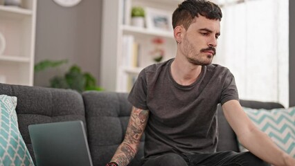 Wall Mural - Young hispanic man talking on smartphone using laptop at home