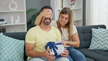 Canvas Print - Man and woman couple surprise with anniversary gift sitting on sofa at home