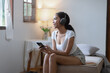 © SOMKID - Young African woman holding smartphone with earphones at home.