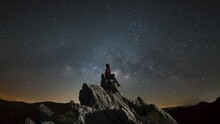 Time-lapse Video Animation Tourist Woman Sitting On The Rock, Doi Pha Tang View Point, Dark Night Sky The Milky Way Galaxy Slowly Moves In Time In The Sky In Chiang Rai, Thailand.