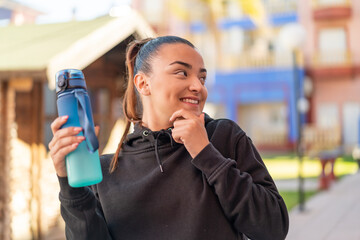 Wall Mural - Young pretty sport woman with a bottle of water at outdoors thinking an idea and looking side