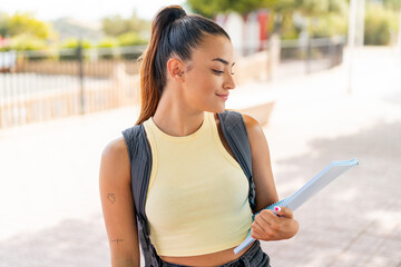 Wall Mural - Young pretty student woman at outdoors with happy expression