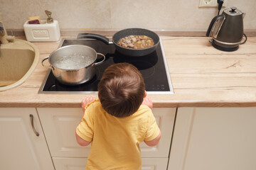 Baby reaches for the hot stove with a pot of boiling water. Child safety issues in the home room. Kid aged two years