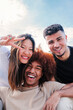 © Jose Calsina - Vertical portrait of group of young multiracial friends hugging and having fun together. Three happy cool buddies smiling looking at camera. Diverse student teenage people laughing bonding at weekend