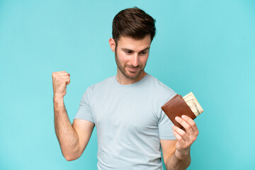 Wall Mural - Young caucasian man holding a wallet isolated on blue background celebrating a victory