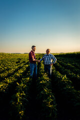 Wall Mural - Two farmers in soy field making agreement with handshake at sunset.