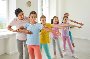 Wall Mural - Female friendly choreographer helping her students girls in doing a dance exercises in studio. Kids doing dance workout. Happy children training in a group choreography class, learning modern dances.