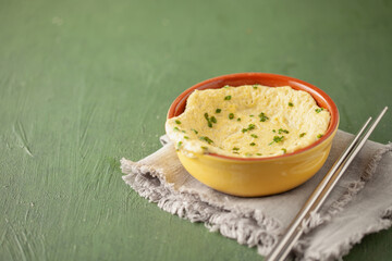 Korean Gyeranjjim Egg Tang with green onions, Korean steamed custard egg in the traditional pot on green table background