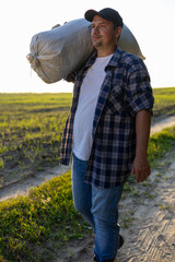 Wall Mural - A tired worker returns from the field with a sack over his shoulder at sunset. A man walks along the field after a hard day's work. Harvesting concept.