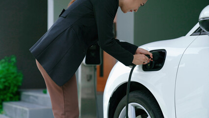 A woman unplugs the electric vehicle's charger at his residence. Concept of the use of electric vehicles in a progressive lifestyle contributes to a clean and healthy environment.