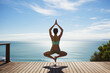 A picture of a woman practicing yoga on a wooden deck with the ocean in the background.