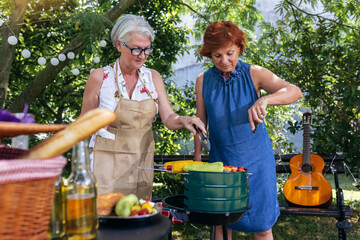 Elderly people are making barbeque, drinking beverages, making memories, and laughing.