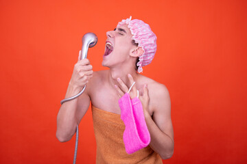 Wall Mural - Funny guy in a pink cap poses on an orange background and washes in the shower.