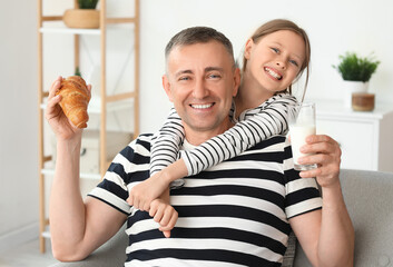 Canvas Print - Little girl and her father with croissant drinking milk in living room