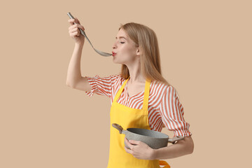 Wall Mural - Young woman with ladle and cooking pot on beige background