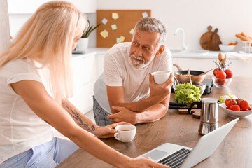 Canvas Print - Mature couple with laptop drinking coffee in kitchen