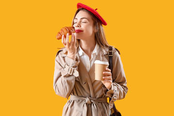 Poster - Beautiful stylish young woman in beret with tasty croissant and cup of coffee on yellow background