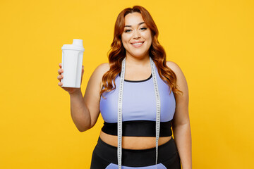 Wall Mural - Satisfied smiling fun young chubby plus size big fat fit woman wear blue top warm up training hold in hand protein cocktail isolated on plain yellow background studio home gym. Workout sport concept.