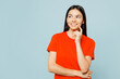 Young latin woman she wear orange red t-shirt casual clothes put hand prop up on chin, lost in thought and conjectures isolated on plain pastel blue cyan background studio portrait. Lifestyle concept.