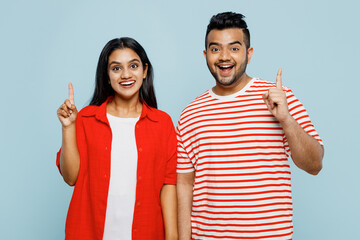 Young smart couple two friends family Indian man woman wear red casual clothes t-shirts together holding index finger up with great new idea isolated on pastel plain light blue cyan color background.
