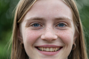 Portrait of a beautiful happy girl with blond hair and freckles looking at the camera and smiling charmingly, closeup, outdoors