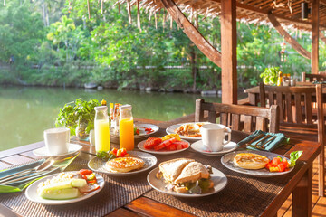 Breakfast table near lake in Asian resort. Delicious meal with fresh fruits, healthy green salad, and organic coffee. Concept of vacation and tropical cuisine.