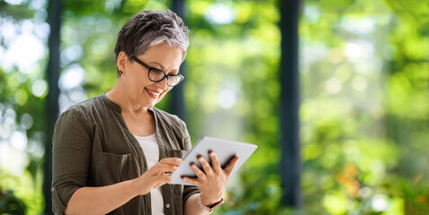 Positive middle aged lady using digital tablet, reading news online