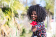 Young, beautiful black woman with afro hair holds a red flower in her hands. The beautiful woman is happy and smiling.