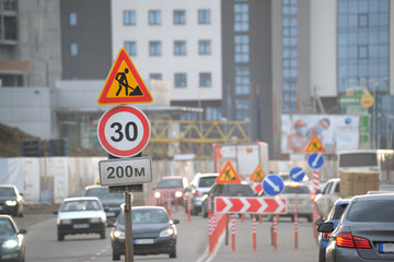 Roadworks warning traffic signs of construction work on city street and slowly moving cars