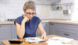 A sad woman looks sadly at money and utility bills.A woman in a blue dress sits in the kitchen counting money on a calculator, writes and pays online.