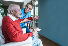 Smiling Nurse Helping Senior Man And Teaching Exercise At Home