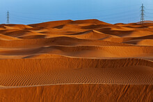 Electricity Pylons Amongst Orange Sand Dunes In Desert, Saudi Arabia