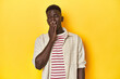 Stylish young African man on vibrant yellow studio background, yawning showing a tired gesture covering mouth with hand.