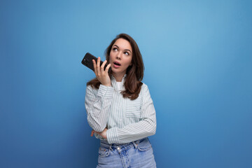 Canvas Print - brunette young woman in a shirt typing a voice message in a smartphone on a studio background with copy pace